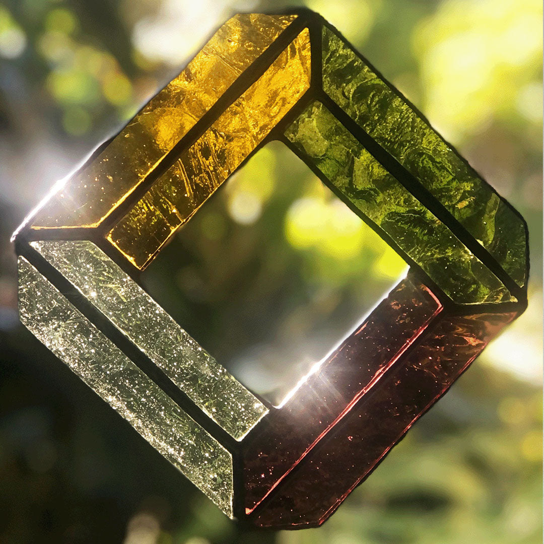 Close up of diamond suncatcher with suns rays filtering in through the coloured translucent glass. This suncatcher is made of four sides, each a different coloured glass including a pale pastel green, a golden yellow, a deeper moss green and a winey purple colour